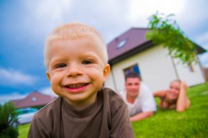 Happy child in front of the house with parents in the background